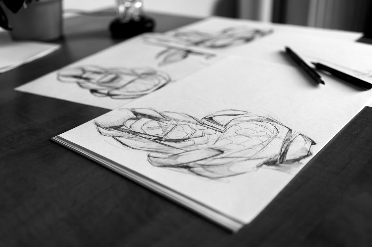 Monochrome image showcasing artistic sketches on paper with pencils on a wooden desk.